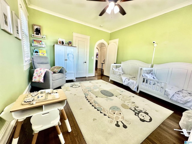 bedroom with baseboards, arched walkways, wood finished floors, and crown molding