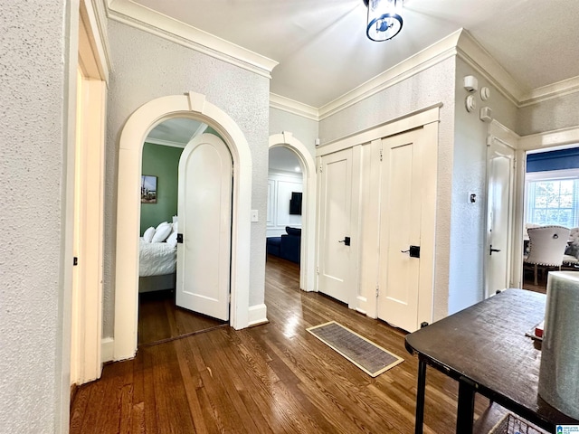 entryway with crown molding, wood finished floors, a textured wall, and arched walkways