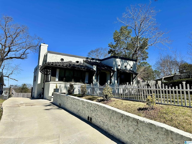 view of front of home featuring a fenced front yard, concrete driveway, a chimney, and a tile roof