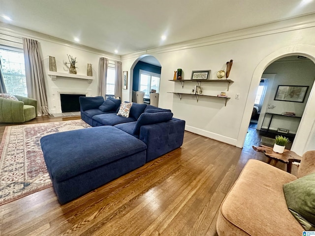 living room featuring baseboards, arched walkways, wood finished floors, and crown molding