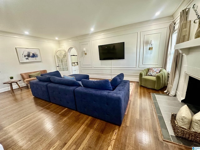 living area featuring hardwood / wood-style floors, baseboards, a fireplace, crown molding, and a decorative wall