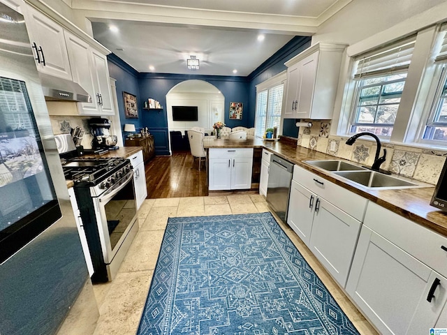 kitchen featuring arched walkways, a sink, white cabinets, appliances with stainless steel finishes, and tasteful backsplash