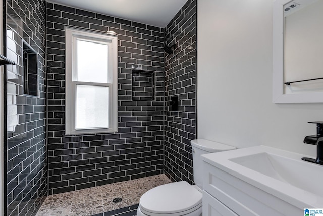 full bathroom with a tile shower, plenty of natural light, toilet, and vanity