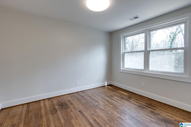 empty room with wood finished floors, baseboards, and visible vents