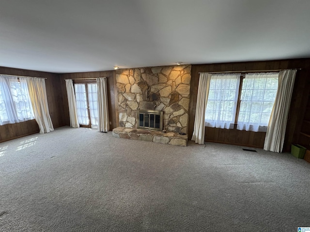 unfurnished living room featuring visible vents, wooden walls, a stone fireplace, and carpet