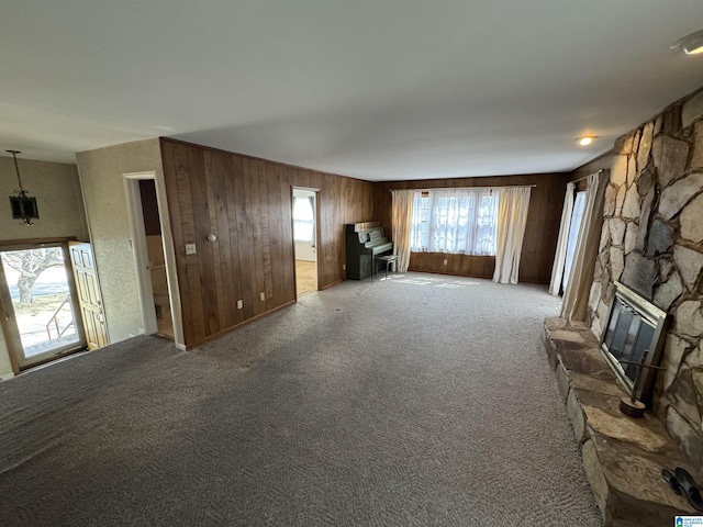 unfurnished living room featuring carpet, a stone fireplace, and wood walls