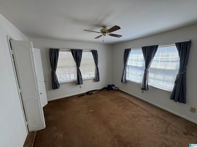 unfurnished room featuring visible vents, plenty of natural light, baseboards, and dark colored carpet