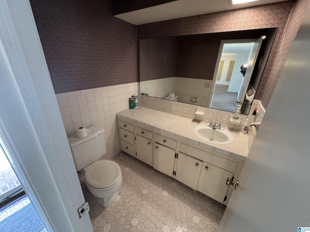 bathroom with vanity, a wainscoted wall, wallpapered walls, tile walls, and toilet