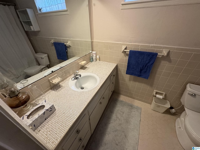 full bathroom featuring toilet, tile walls, wainscoting, tile patterned flooring, and vanity