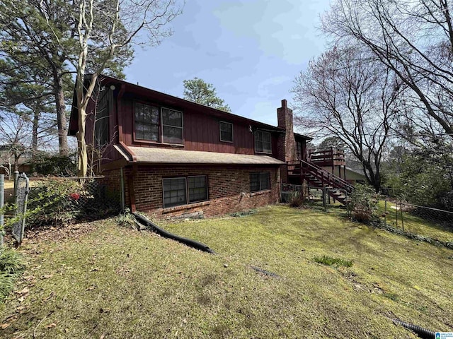 rear view of house featuring brick siding, fence, stairway, a chimney, and a yard