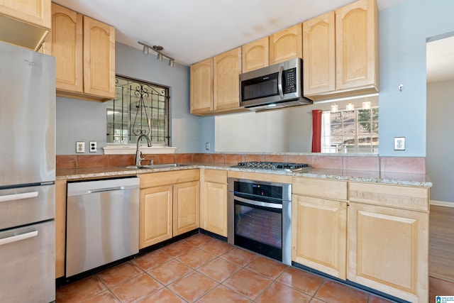 kitchen with a wealth of natural light, light brown cabinets, a sink, appliances with stainless steel finishes, and light stone countertops