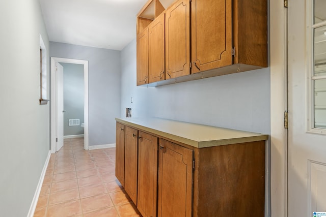 kitchen with light tile patterned floors, baseboards, visible vents, light countertops, and brown cabinets