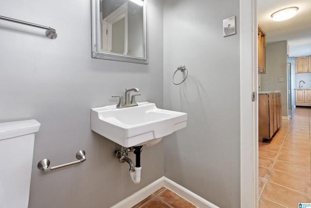 half bathroom with tile patterned flooring, toilet, baseboards, and a sink