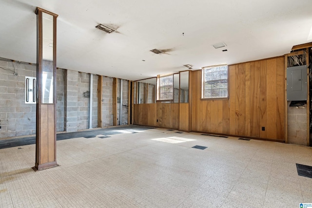 empty room featuring electric panel, wooden walls, concrete block wall, and tile patterned floors