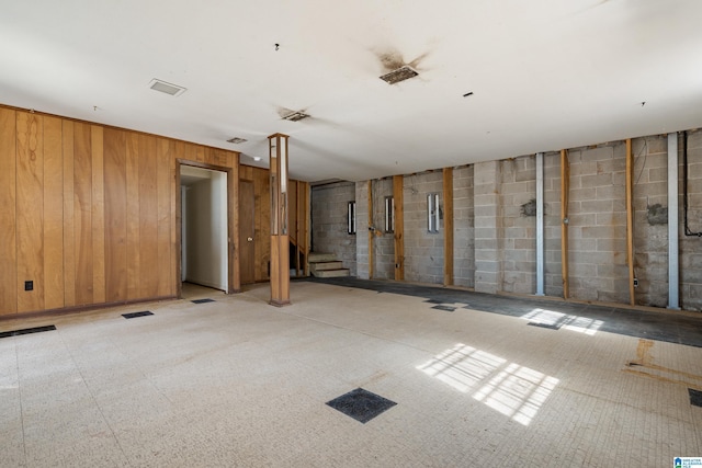 spare room with stairway, concrete block wall, visible vents, and wooden walls