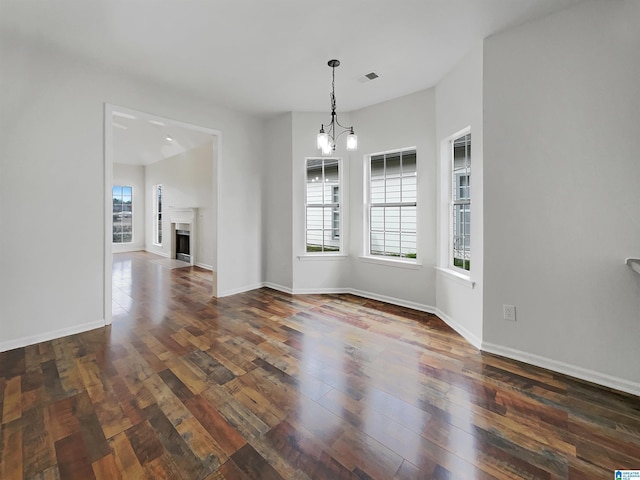 empty room with dark wood-style floors, visible vents, a healthy amount of sunlight, and a fireplace