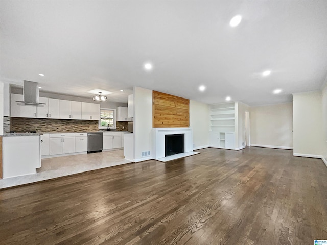 unfurnished living room featuring visible vents, dark wood-type flooring, recessed lighting, a fireplace, and a sink