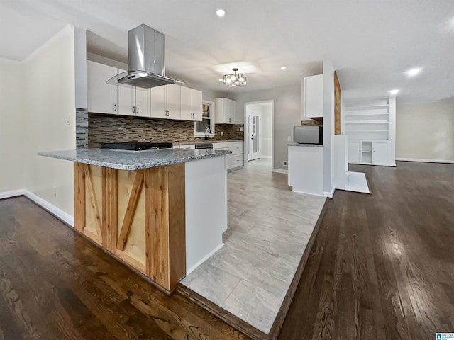 kitchen featuring backsplash, a peninsula, island range hood, white cabinets, and a sink