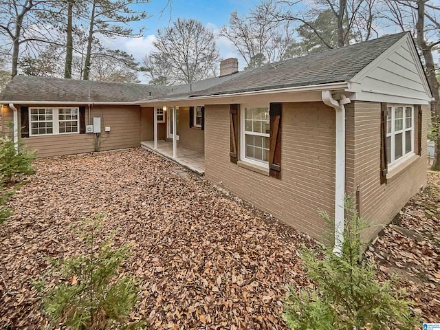 view of side of property featuring a shingled roof, a patio, brick siding, and a chimney