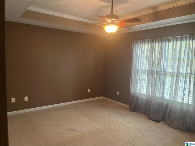 empty room featuring a raised ceiling, crown molding, light colored carpet, and baseboards