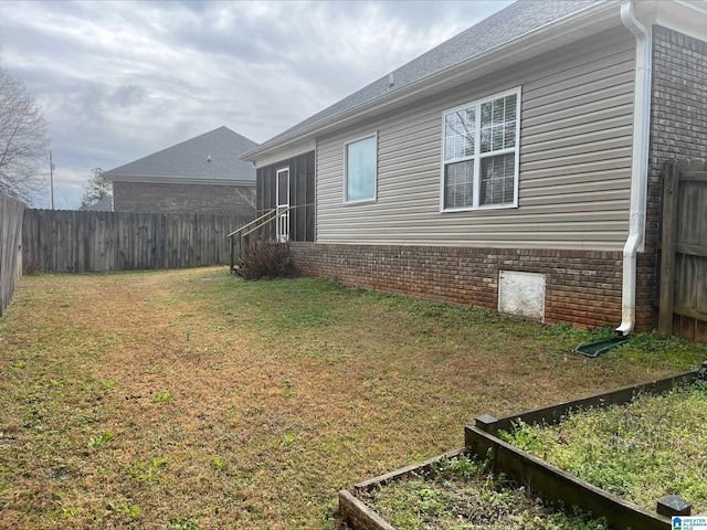 view of side of property featuring a garden, a yard, brick siding, and fence