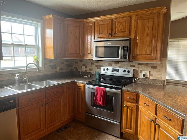 kitchen featuring brown cabinetry, visible vents, a sink, appliances with stainless steel finishes, and tasteful backsplash