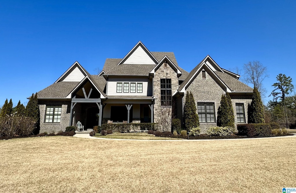 view of front of property with brick siding, stone siding, a front yard, and roof with shingles