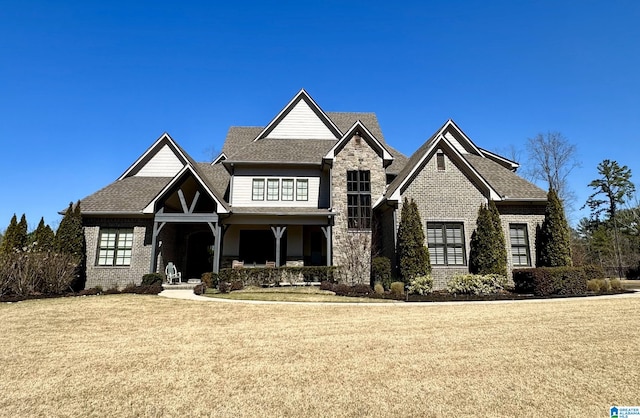 view of front of property with brick siding, stone siding, a front yard, and roof with shingles