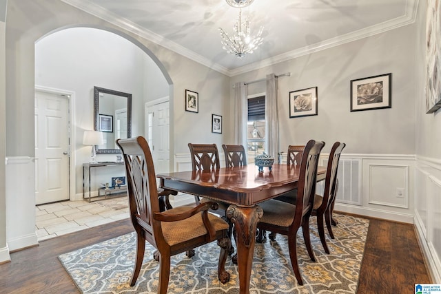 dining space featuring ornamental molding, wainscoting, an inviting chandelier, wood finished floors, and arched walkways