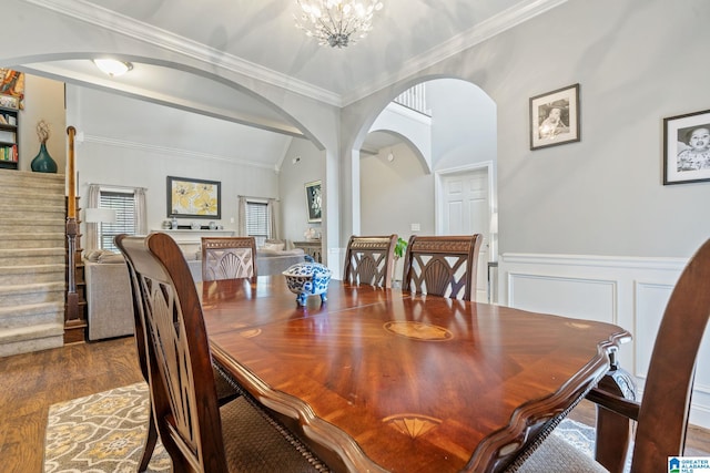 dining space with a wainscoted wall, stairs, wood finished floors, arched walkways, and a notable chandelier