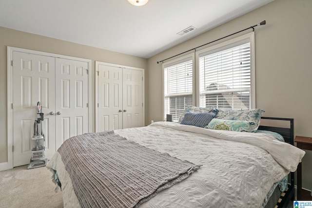 bedroom featuring light carpet, visible vents, two closets, and baseboards