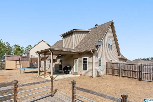 back of property with a trampoline, roof with shingles, a fenced backyard, a patio area, and a ceiling fan