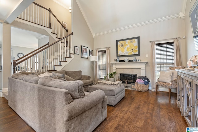 living area with high vaulted ceiling, ornamental molding, a tiled fireplace, dark wood finished floors, and stairs