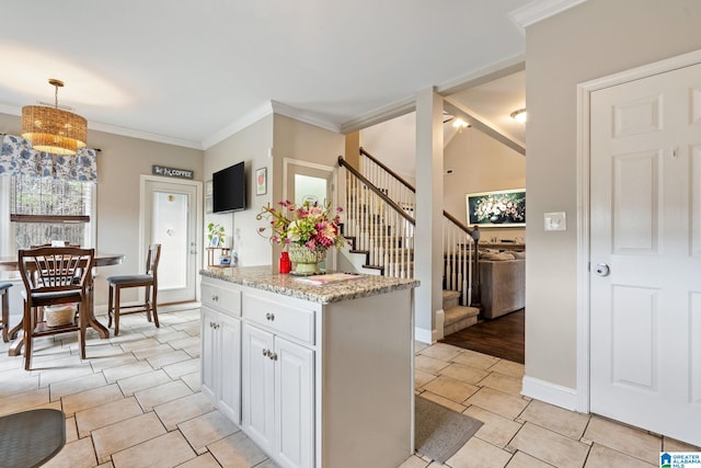 kitchen with light tile patterned floors, light stone countertops, hanging light fixtures, white cabinets, and crown molding