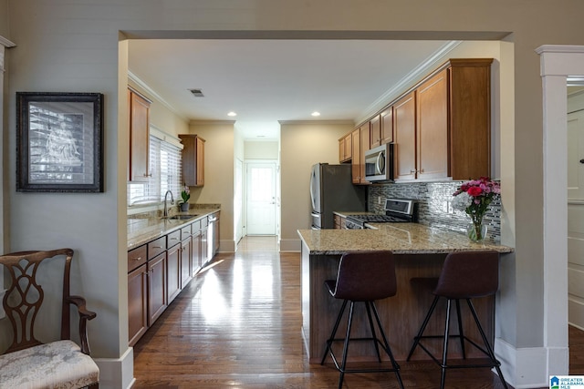 kitchen with a sink, light stone counters, appliances with stainless steel finishes, a breakfast bar area, and dark wood-style flooring