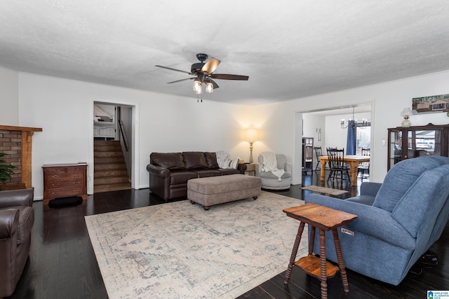 living room featuring dark wood finished floors, ceiling fan with notable chandelier, a textured ceiling, and stairs