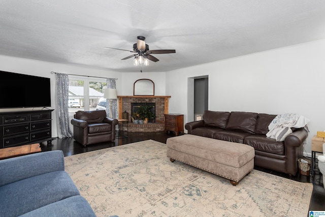 living area with wood finished floors, a textured ceiling, a brick fireplace, and ceiling fan