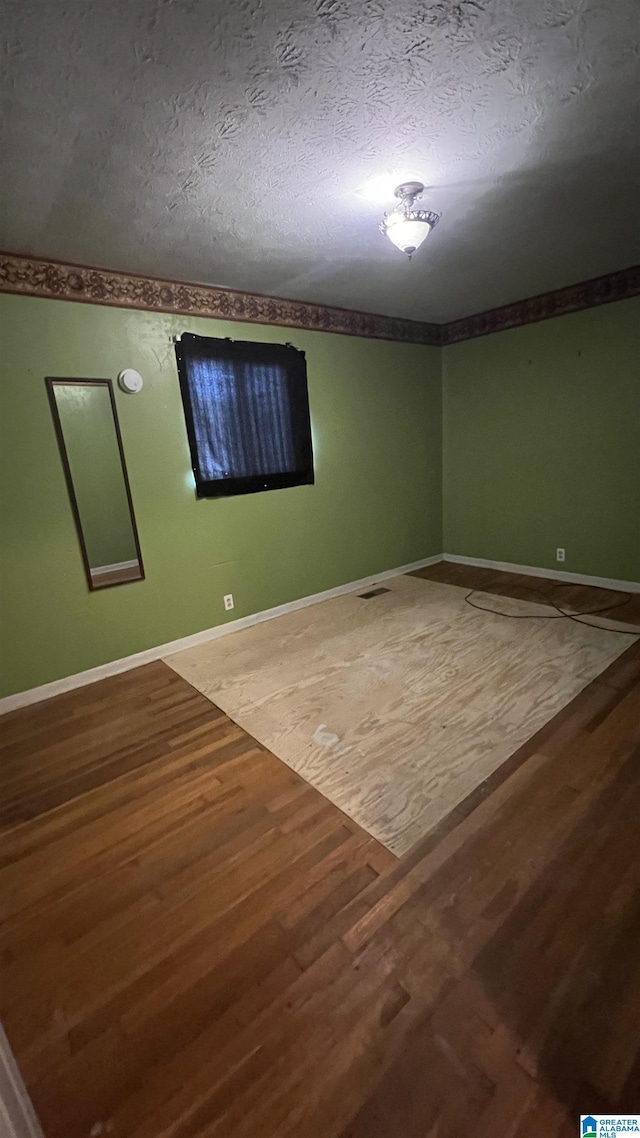 empty room featuring a textured ceiling, crown molding, baseboards, and wood finished floors