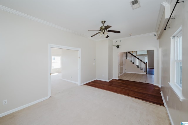 empty room with visible vents, crown molding, baseboards, carpet, and stairway