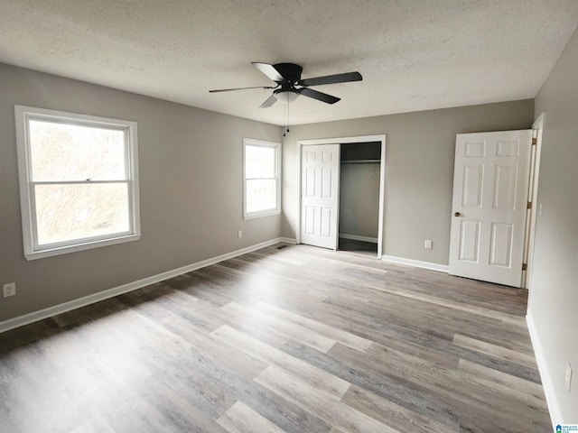 unfurnished bedroom featuring wood finished floors, baseboards, a closet, and a textured ceiling