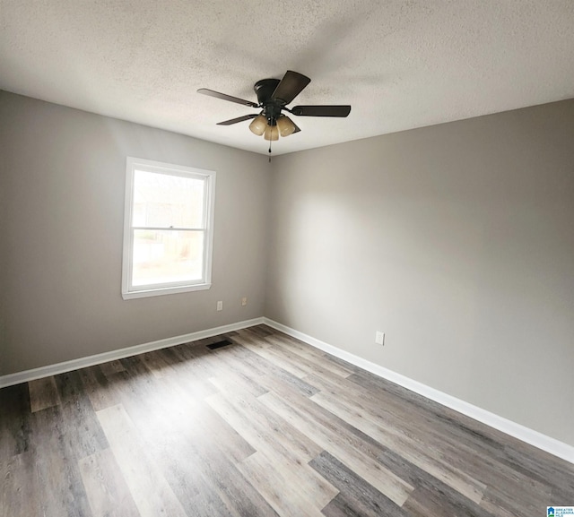 empty room with ceiling fan, visible vents, baseboards, and wood finished floors