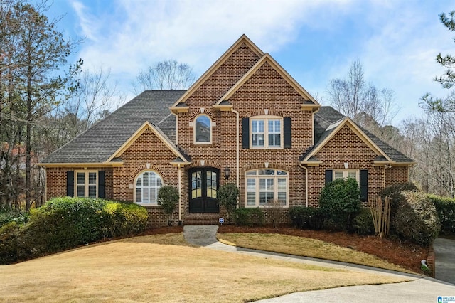 traditional-style home with brick siding, french doors, a shingled roof, and a front lawn