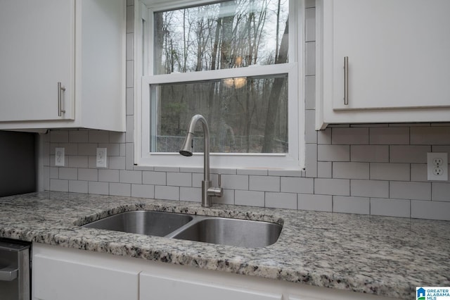 kitchen featuring a sink, light stone counters, backsplash, and white cabinets