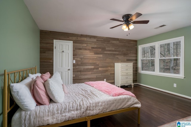 bedroom with wooden walls, wood finished floors, visible vents, and baseboards