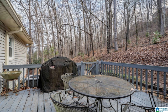 wooden terrace with grilling area, a forest view, outdoor dining area, and central AC