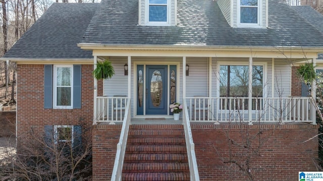 property entrance featuring roof with shingles, a porch, and brick siding