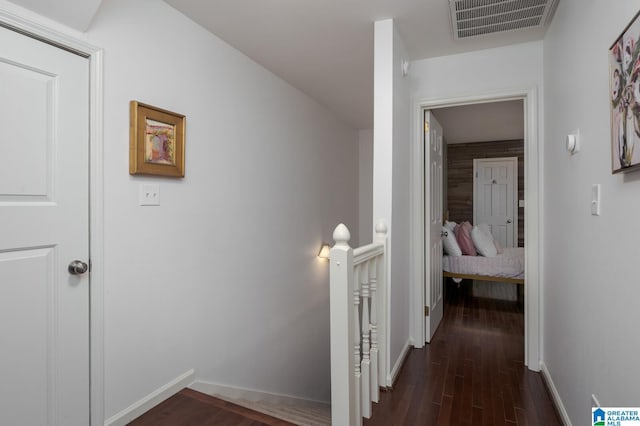 hallway with an upstairs landing, visible vents, baseboards, and dark wood-style floors