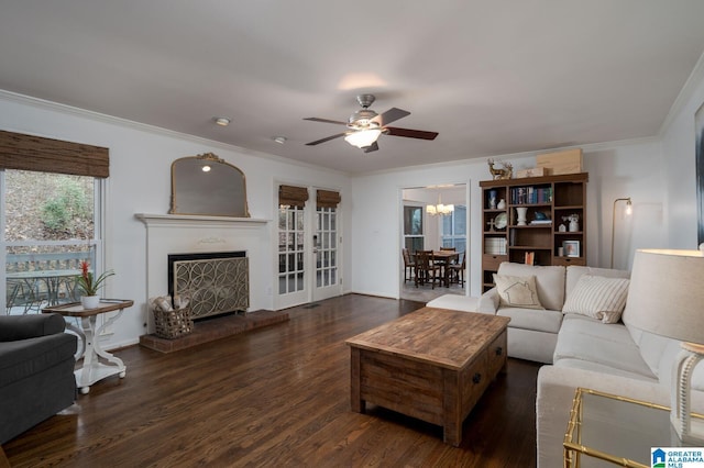 living area featuring a fireplace with raised hearth, ornamental molding, ceiling fan with notable chandelier, wood finished floors, and baseboards