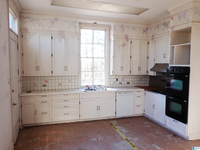 kitchen with tile countertops, a sink, under cabinet range hood, dobule oven black, and dishwasher