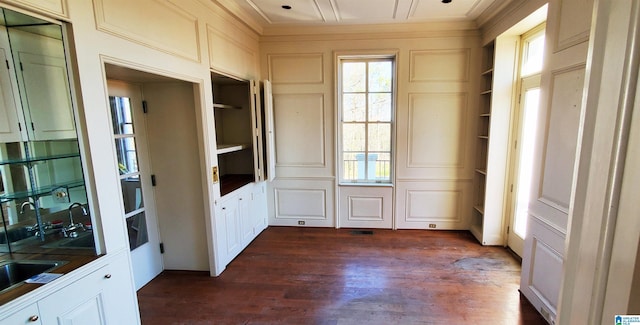 doorway to outside with a decorative wall, built in shelves, crown molding, and dark wood-style flooring